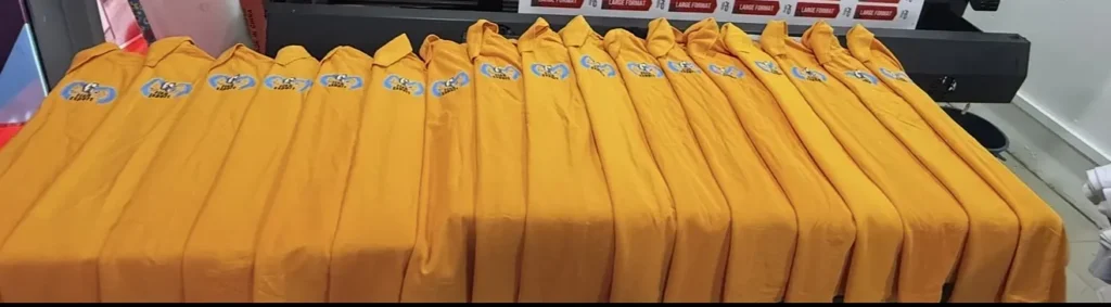 Row of orange polo shirts with a printed blue chest logo laid out on a table