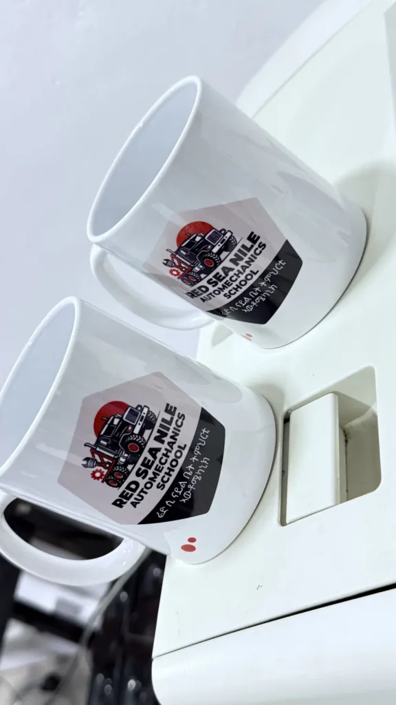 Two white mugs printed with the Red Sea Nile Automechanics School logo